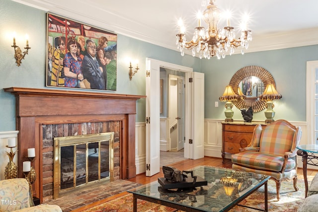 sitting room with a fireplace, wood finished floors, a wainscoted wall, ornamental molding, and a chandelier