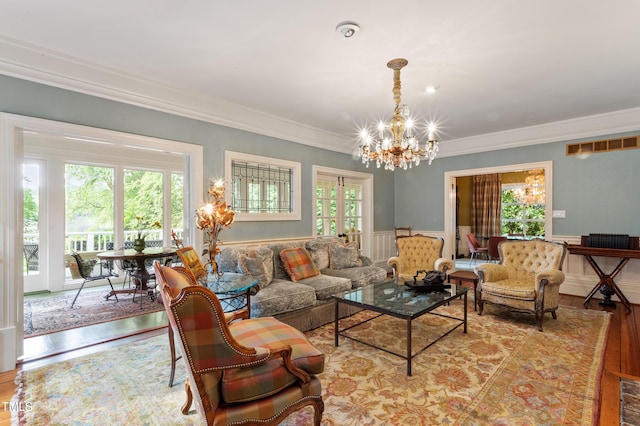 living area with a chandelier, ornamental molding, wood finished floors, and wainscoting