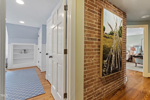 corridor featuring light wood-style floors and brick wall