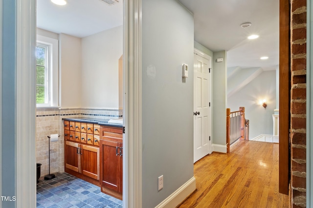 corridor with an upstairs landing, recessed lighting, light wood-style flooring, and tile walls