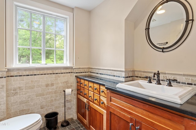 bathroom with tile walls, toilet, wainscoting, tile patterned flooring, and vanity