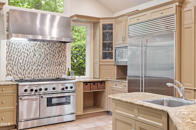 kitchen with built in appliances, a sink, cream cabinetry, decorative backsplash, and wall chimney range hood