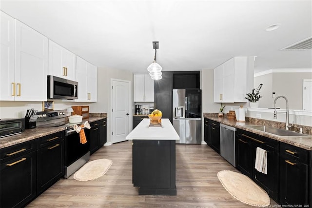 kitchen with a center island, a sink, dark cabinetry, stainless steel appliances, and light wood-style flooring