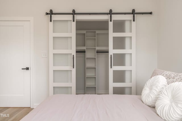 bedroom with a barn door, wood finished floors, and a closet