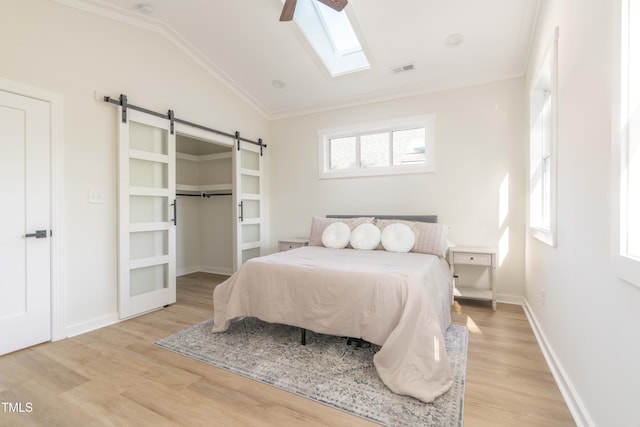 bedroom featuring a barn door, light wood finished floors, vaulted ceiling, a skylight, and ornamental molding