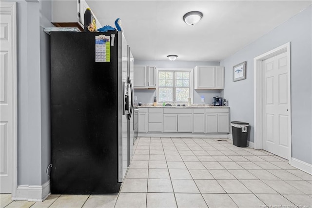 kitchen with light countertops, stainless steel refrigerator with ice dispenser, light tile patterned flooring, white cabinetry, and a sink