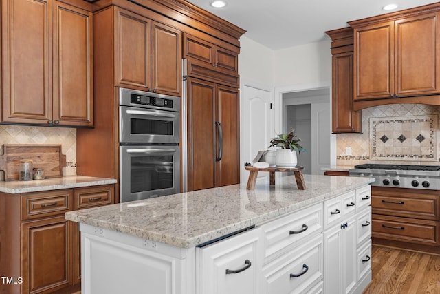kitchen with stainless steel appliances, decorative backsplash, brown cabinetry, and light stone counters