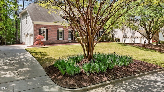 view of front of home featuring roof with shingles, driveway, a garage, brick siding, and a front yard
