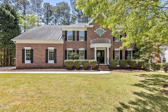 view of front facade with brick siding, a balcony, a shingled roof, and a front yard