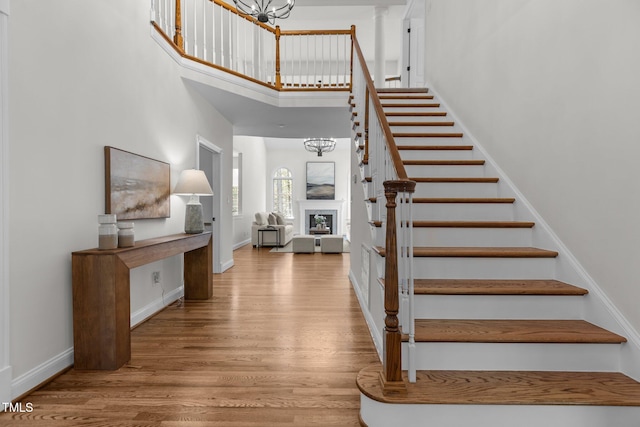 stairs with a chandelier, wood finished floors, a towering ceiling, and baseboards