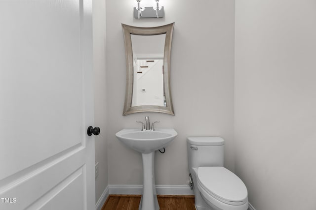 bathroom featuring baseboards, wood finished floors, a sink, and toilet