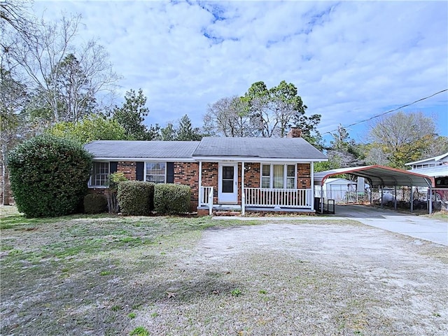 view of front of home with brick siding, covered porch, a chimney, a carport, and driveway