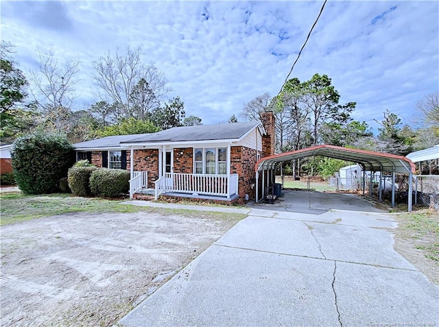 view of front of house with a porch, a detached carport, concrete driveway, brick siding, and a chimney