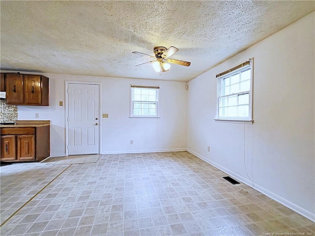 interior space with visible vents, baseboards, a textured ceiling, and ceiling fan