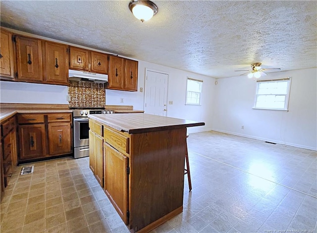 kitchen with brown cabinets, under cabinet range hood, stainless steel electric range oven, light floors, and ceiling fan