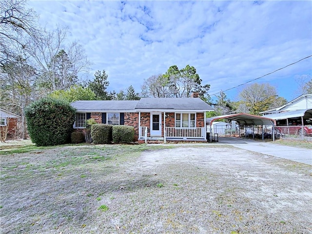 ranch-style house with a detached carport, a porch, a chimney, concrete driveway, and brick siding