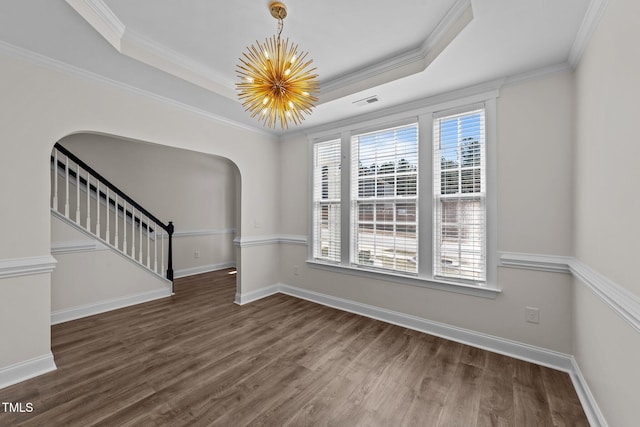 spare room featuring wood finished floors, arched walkways, a chandelier, and a raised ceiling
