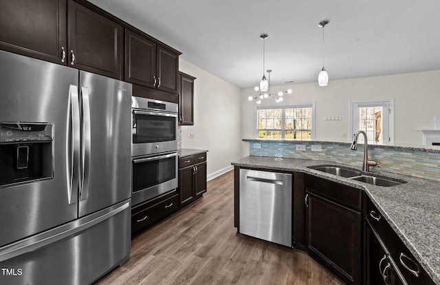 kitchen with dark wood finished floors, stainless steel appliances, an inviting chandelier, a sink, and light stone countertops