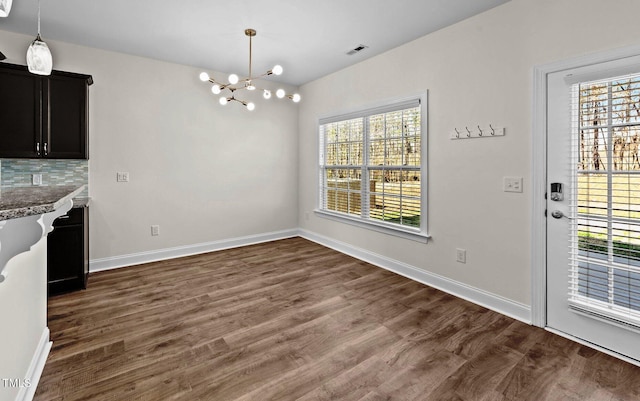 unfurnished dining area with plenty of natural light, visible vents, an inviting chandelier, and dark wood-type flooring