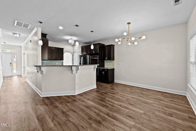 kitchen with oven, a breakfast bar area, an inviting chandelier, refrigerator with ice dispenser, and visible vents