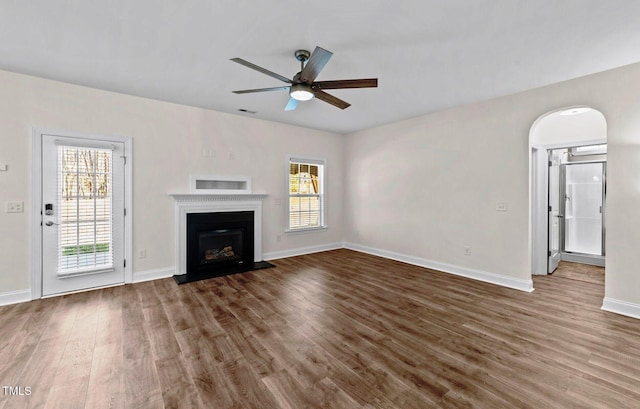 unfurnished living room with baseboards, a ceiling fan, wood finished floors, and a fireplace with raised hearth