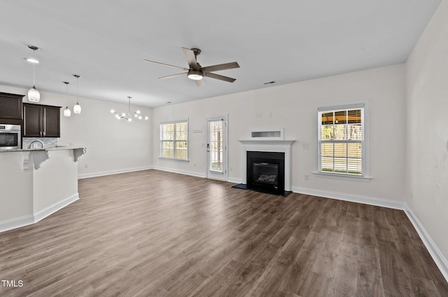 unfurnished living room with visible vents, baseboards, a glass covered fireplace, dark wood-style flooring, and ceiling fan with notable chandelier