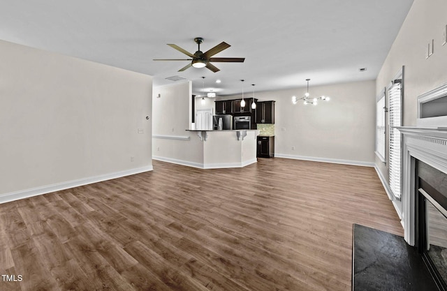 unfurnished living room with a fireplace with flush hearth, baseboards, dark wood-style flooring, and ceiling fan with notable chandelier