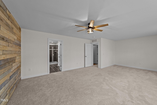 empty room featuring light carpet, baseboards, visible vents, ceiling fan, and wooden walls