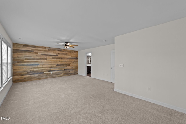 carpeted spare room featuring baseboards, a ceiling fan, and wooden walls