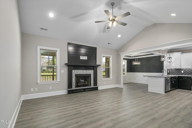 unfurnished living room with ceiling fan, visible vents, vaulted ceiling, and light wood finished floors