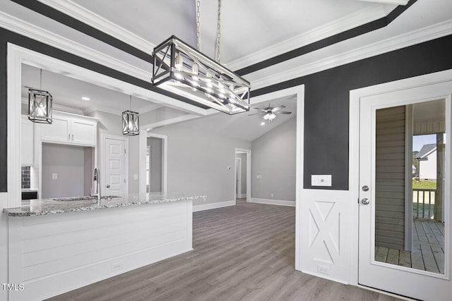 kitchen with ornamental molding, a sink, light stone counters, white cabinets, and wood finished floors