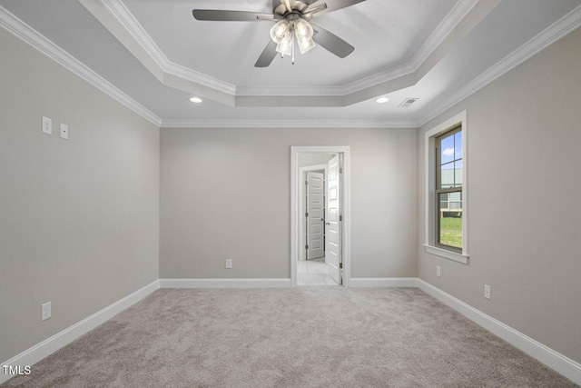 unfurnished room with a tray ceiling, crown molding, carpet flooring, baseboards, and ceiling fan