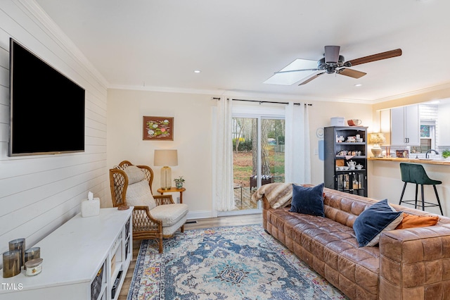 living area with crown molding, a ceiling fan, wood walls, light wood-style flooring, and a skylight