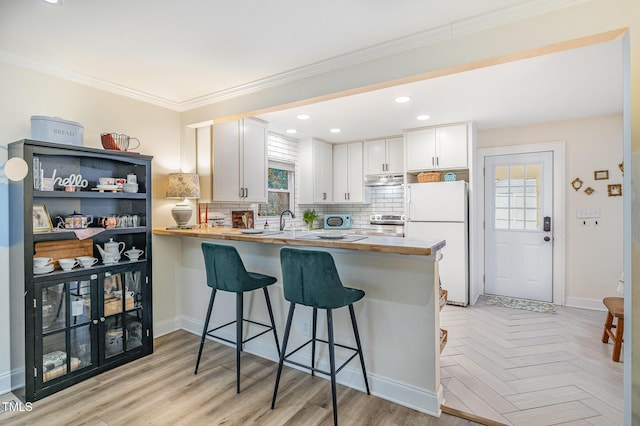 kitchen featuring tasteful backsplash, plenty of natural light, a breakfast bar area, freestanding refrigerator, and a peninsula