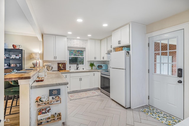 kitchen featuring a kitchen breakfast bar, decorative backsplash, white cabinets, freestanding refrigerator, and electric range