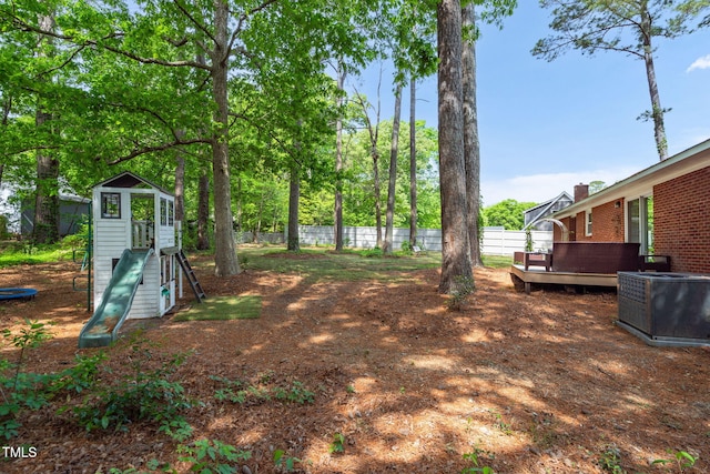view of yard featuring fence, central AC unit, a wooden deck, and a playground