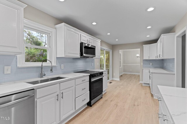 kitchen with light wood-style flooring, baseboards, stainless steel appliances, white cabinetry, and a sink