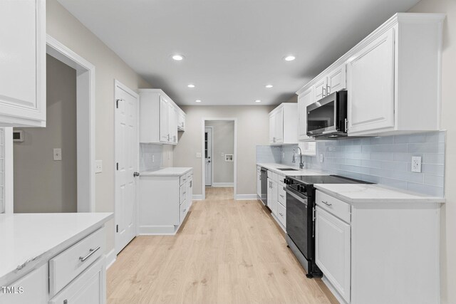kitchen featuring light countertops, a sink, light wood finished floors, stainless steel appliances, and white cabinets