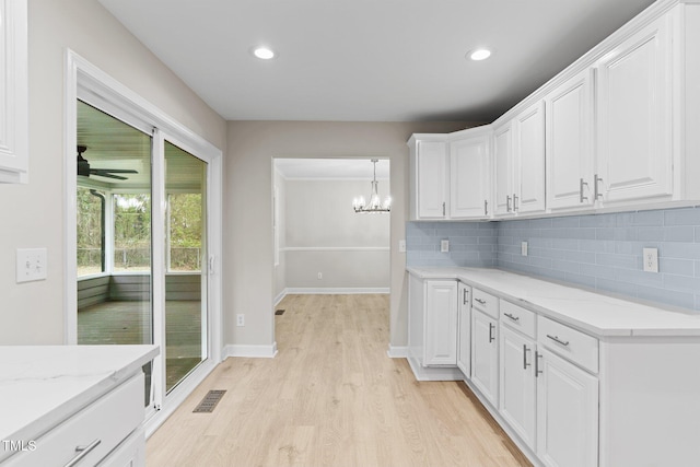 kitchen with white cabinetry, light wood-type flooring, backsplash, visible vents, and light stone countertops