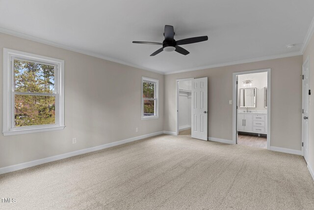 unfurnished bedroom featuring crown molding, a spacious closet, baseboards, light carpet, and ensuite bathroom