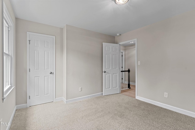 unfurnished bedroom featuring multiple windows, baseboards, and light colored carpet