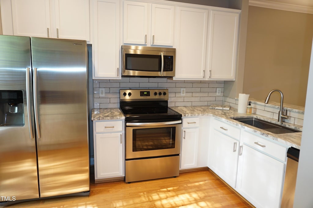 108 W Savannah Ridge Rd, Holly Springs, NC 27540 - kitchen featuring appliances with stainless steel finishes, crown molding, white cabinets, light stone counters, and light wood-type flooring