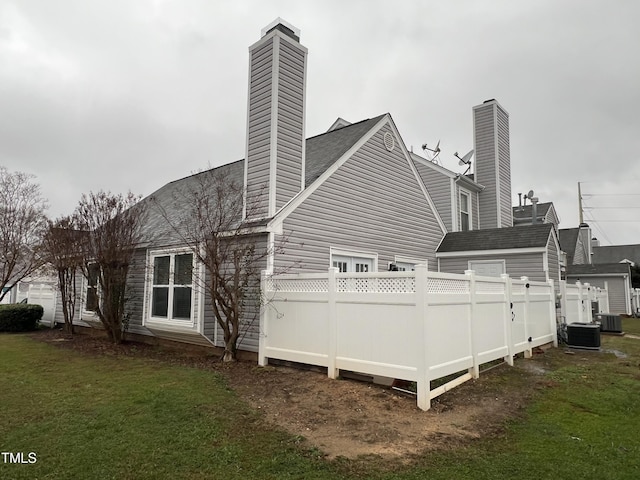 rear view of house with cooling unit, a lawn, a chimney, and fence