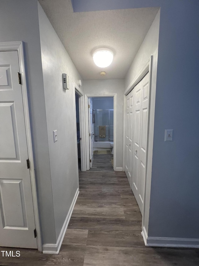 hallway featuring dark wood finished floors, baseboards, and a textured ceiling