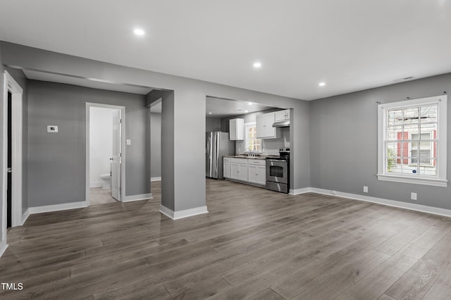 unfurnished living room with dark wood-style flooring, a sink, baseboards, and recessed lighting