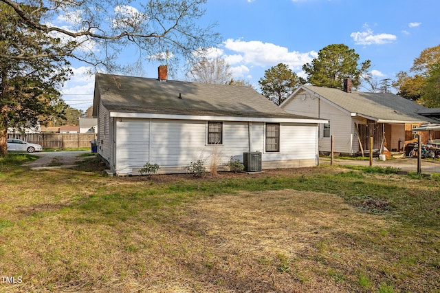 back of property with fence, central AC unit, a yard, and a chimney
