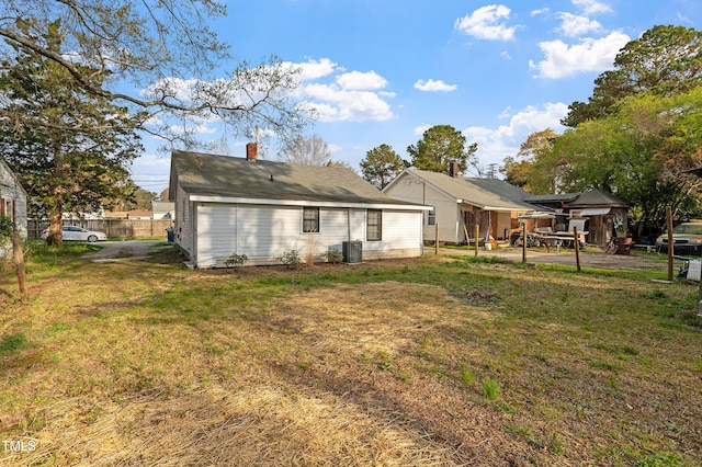 back of house featuring a lawn, a chimney, central AC unit, and fence