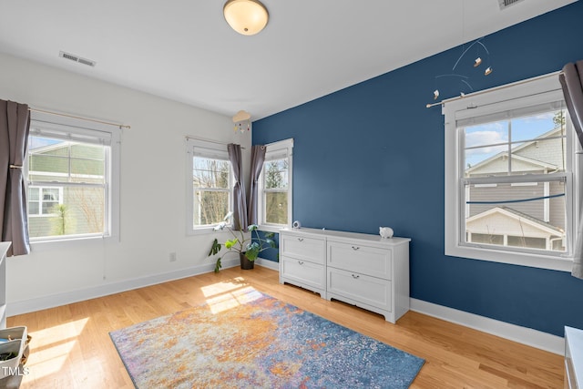 bedroom featuring light wood-style floors, baseboards, multiple windows, and visible vents