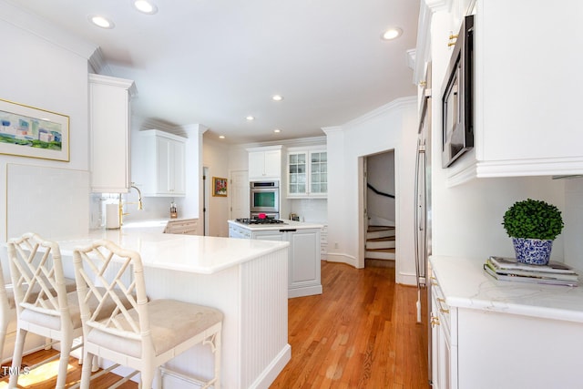 kitchen featuring a breakfast bar, a peninsula, light wood-style flooring, a sink, and oven