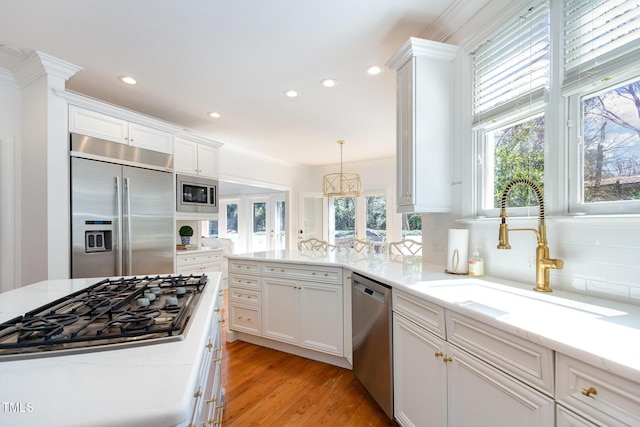 kitchen with light wood finished floors, backsplash, built in appliances, white cabinets, and a sink
